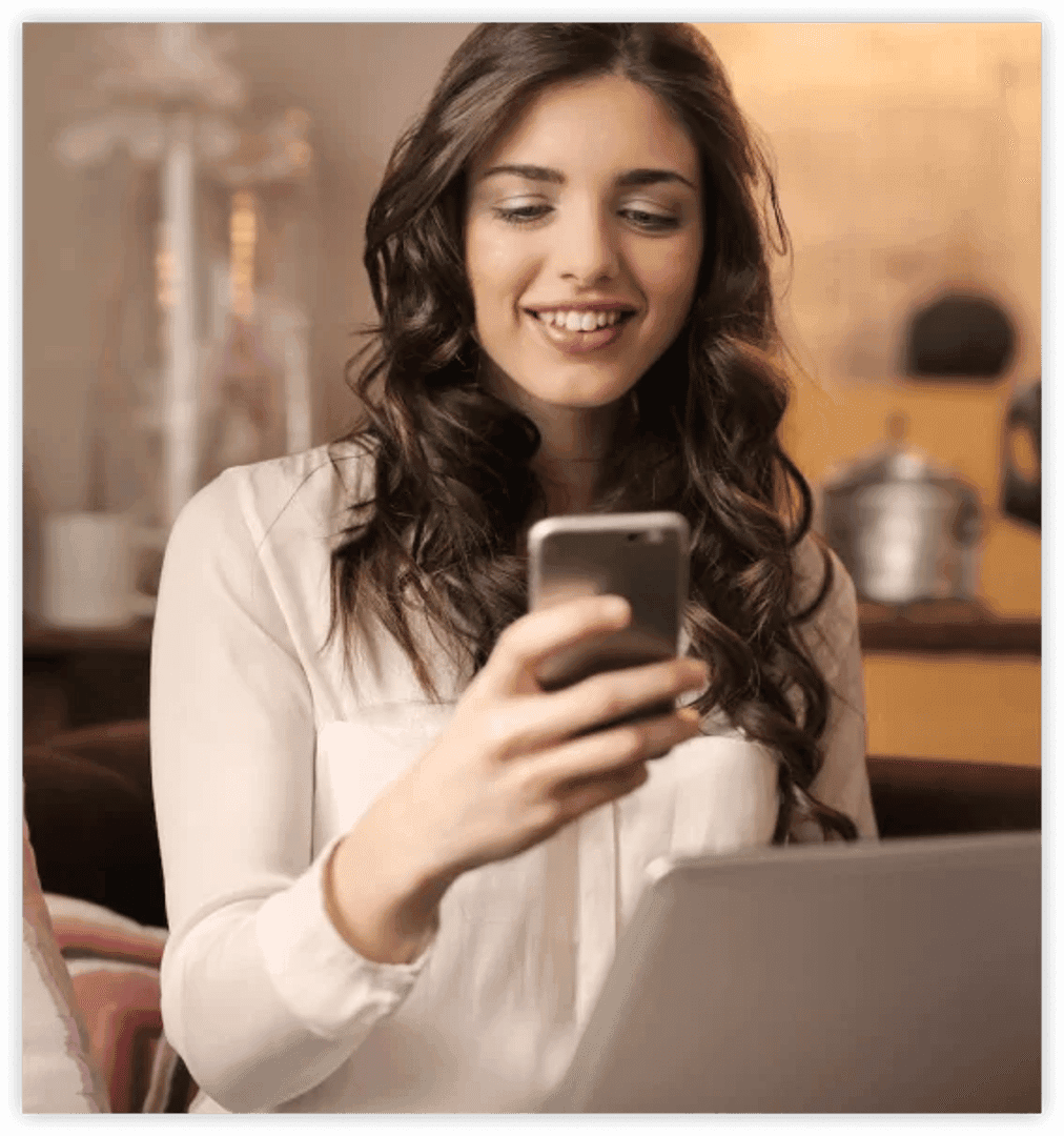 a girl working on a laptop with mobile phone in her hand looking at mobile screen